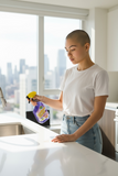 A woman is cleaning a kitchen counter with a bottle of Green Scene Lavalosso cleaner.