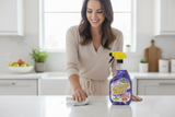 A woman is cleaning a kitchen counter with a bottle of Green Scene Lavalosso cleaner.